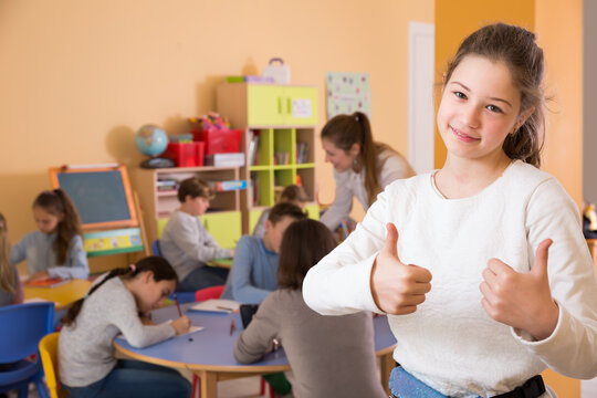 Portrait of positive schoolgirl and children drawing in classroom
