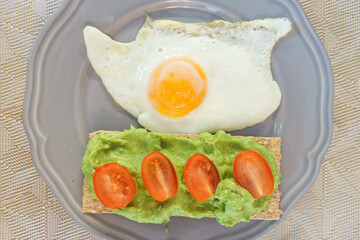 Simple and delicious breakfast: fried eggs on rye bread with guacomole, avocado puree and cherry tomato slices.