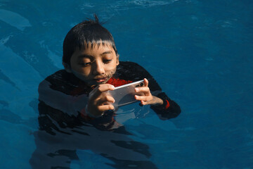 Asian boy using smartphone in the swimming pool. Technology, summer and holiday concept