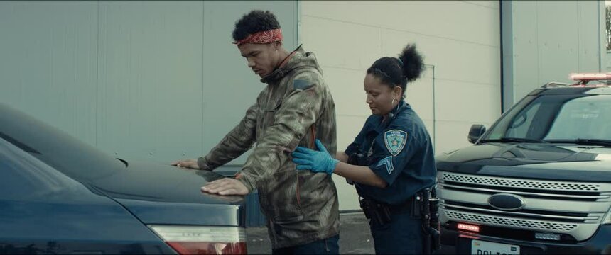 Police officer searches a suspect near a police vehicle in the street. Lights flashing in the background