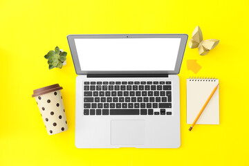 Modern laptop with stationery and cup of coffee on color background