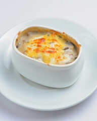 Roasted vegetables, potatoes, mushrooms and cheese in a pot. Baked dinner in a white pot. Delicious meal for dinner.