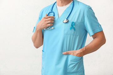 Male doctor with blue ribbon on light background. Prostate cancer awareness concept