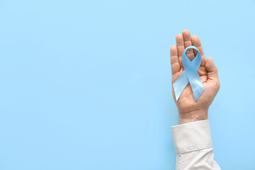Male hand with blue ribbon on color background. Prostate cancer awareness concept