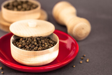 a dried aromatic black pepper in wooden bowl, natural condiment, peppercorns culinary spice on red plate, space for text