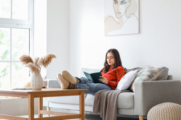 Beautiful young woman reading book at home