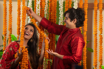 young couple having fun with each other while decorating with flower garlands	