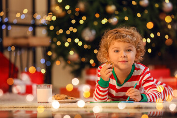 Cute little child eating cookies while writing letter to Santa at home