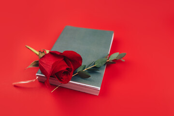 Beautiful red rose with a twig with lying leaves on a black notebook, a gift for any occasion, a gift to your loved one on a red background