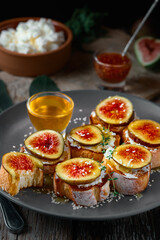 Fruit toast on toasted baguette with figs and goat cheese on a plate with honey, sesame seeds and walnuts. Fresh toast with figs and garnished with thyme leaves. Close-up.