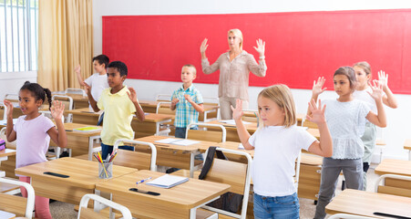 Fototapeta na wymiar Cheerful preteen pupils doing little warm-up in class with female teacher at lesson in elementary school