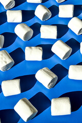 Many rows of white marshmallows cylindrical form lies on blue background. Pattern of unhealthy...