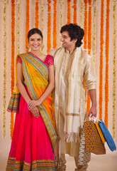  young couple happily standing together in traditional wear holding gifts while the man looks at...