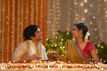 Young couple laughing together while lighting diyas for Diwali	
