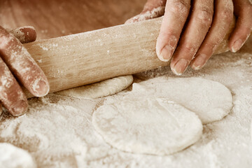the cook rolls out the dough, baker's hands, dough, hands in flour