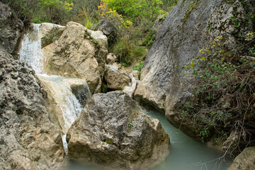 A waterfall in a river in South France, between dark rocks. Forms white scum. Early autumnal colors. Picture in landscape mode.