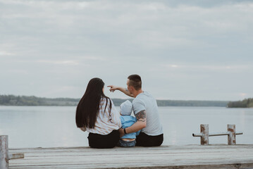Fototapeta premium Young happy family sitting on the pier in the summer