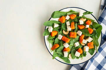 Bright autumn salad with pumpkin, spinach and feta cheese on a light concrete background. Diet healthy food. View from above. A place for text.