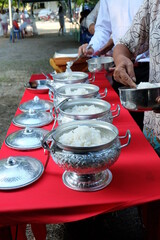 Scoop rice into a Thai patterned aluminum bowl for offering to monks on religious days.