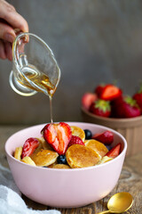 Pancake porridge, mini pancakes in a bowl with maple syrup.Dutch mini pancakes are called strawberry potato pancakes.Syrup is poured onto mini pancakes with strawberries, blueberries.World food day