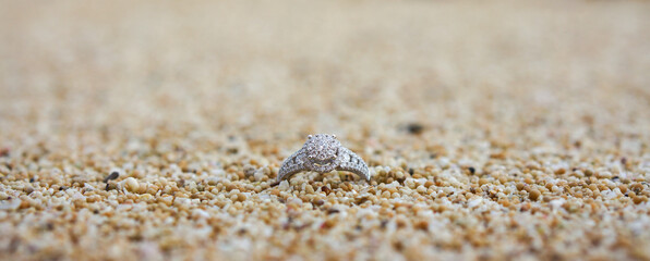 Close up of single diamond ring in sand grain with thin depth of field bokeh for anniversary, honeymoon, romance, relationship concept.
