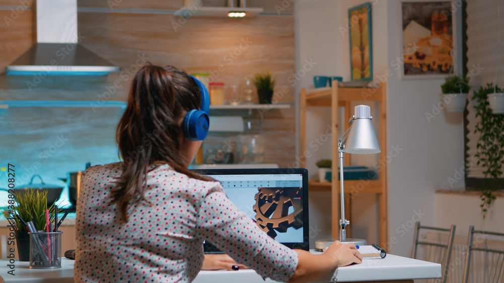 Poster architect with wireless headset using laptop while working at home at night sitting in the kitchen. 