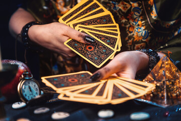 Astrology and cartomancy. A fortune teller holds a fan of Tarot cards. On the table are runes. Close-up of hands