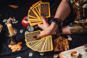 Astrology and esotericism. A fortune teller holds a fan of Tarot cards. On the table are runes and magic glass pyramid. Close-up of hands. Top view