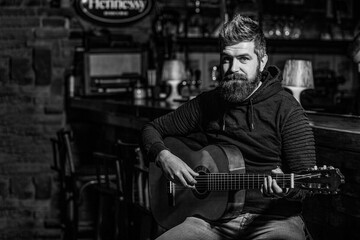 Fototapeta na wymiar Play the guitar. Beard hipster man sitting in a pub. Music concept. Bearded guitarist plays. Black and white