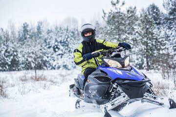 Fototapeta na wymiar Man driving snowmobile in snowy forest. Man on snowmobile in winter mountain. Snowmobile driving