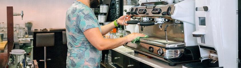 Young waiter cleaning the coffee machine in a cafeteria