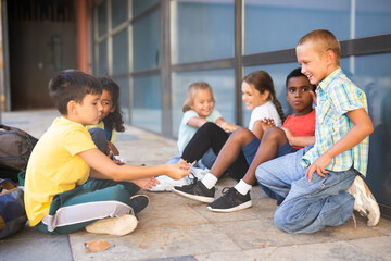 Multiethnic group of cheerful preteens resting outdoors in schoolyard during break in lessons. Back school concept .