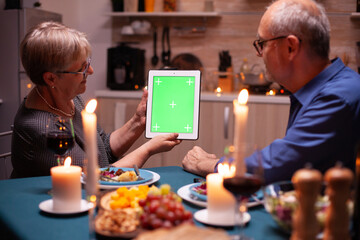 Elderly husband and wife looking at tablet pc with green mockup. Aged people looking at green...