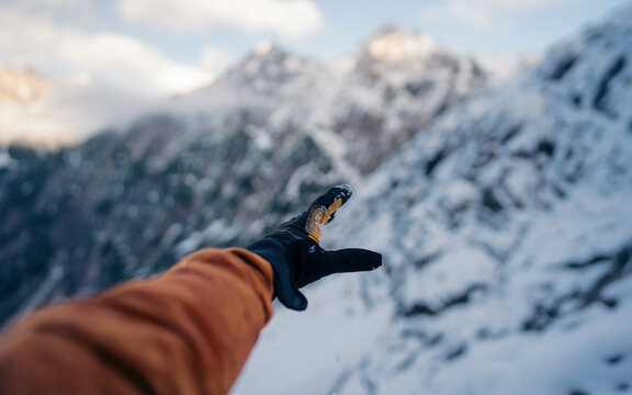 Hand winter sport glove on snow, ice and rock in the background. Snow and ice, blue sky. Winter climbing, hiking and ski touring. Point of view of an climbing tool in a hand of an alpinist.