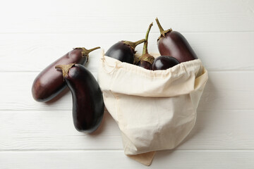 Cotton bag with fresh eggplants on wooden background