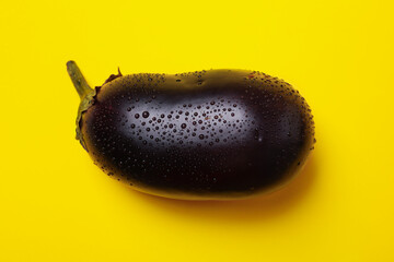 Fresh raw eggplant with water drops on yellow background