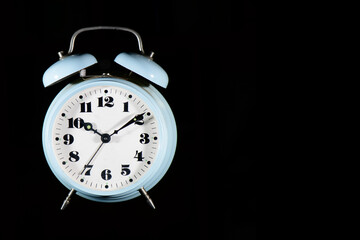Classic table alarm clock in light blue color on a black background