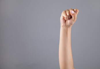 Hand of woman with clenched fist on gray background.
