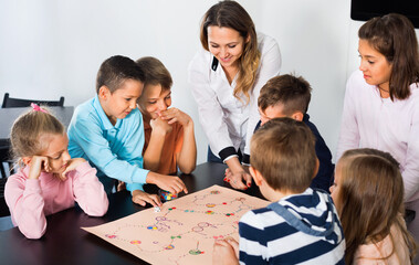 Cheerful boys and little girls playing at board game indoors