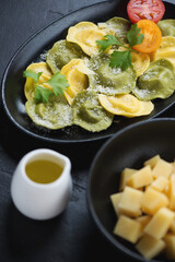 Italian ravioli filled with burrata cheese and green basil, vertical shot over black stone background, close-up
