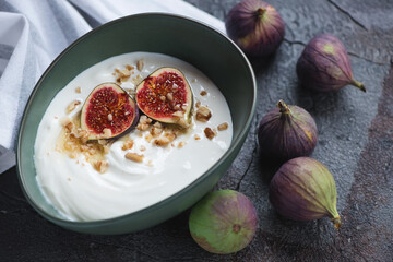 Greek yogurt served with sliced figs, walnuts and honey in a green bowl, studio shot on a grey stone background