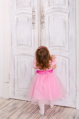 Fototapeta na wymiar little girl in a pink dress. little girl opens the door. Child on tiptoe. The girl reaches for the doorknob.