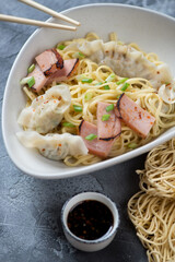 Asian dry wonton noodles or egg noodles served with wontons and chinese bbq pork slices, closeup, vertical shot