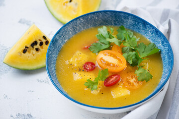 Blue plate with gazpacho made of yellow tomatoes and yellow watermelon, studio shot on a white concrete background