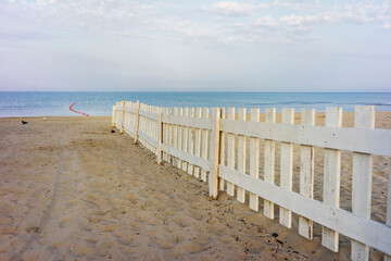 White wooden fence on a sandy beach on the background of the sea at dawn.