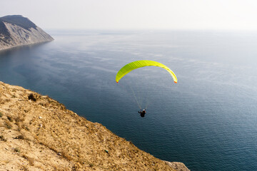 A paraglider flies over mountains and sea in a blue sky on a Sunny summer day.