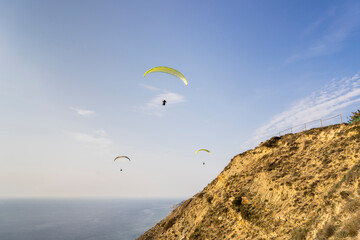A paraglider flies over mountains and sea in a blue sky on a Sunny summer day.