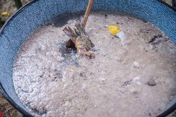 Mixing and cooking fish soup in big caldron made on fire