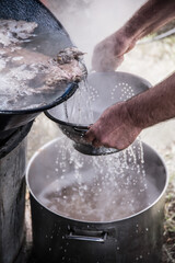 Decanting and filtering hot water from homemade fish soup cooked in a countryside
