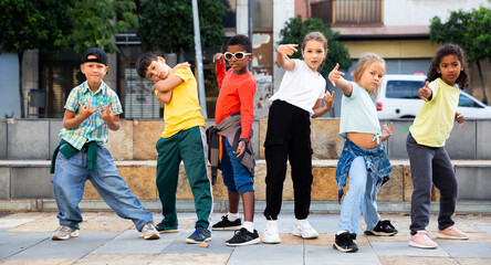 Cheerful preteen boys and girls breakdancers dancing on city street on summer day.